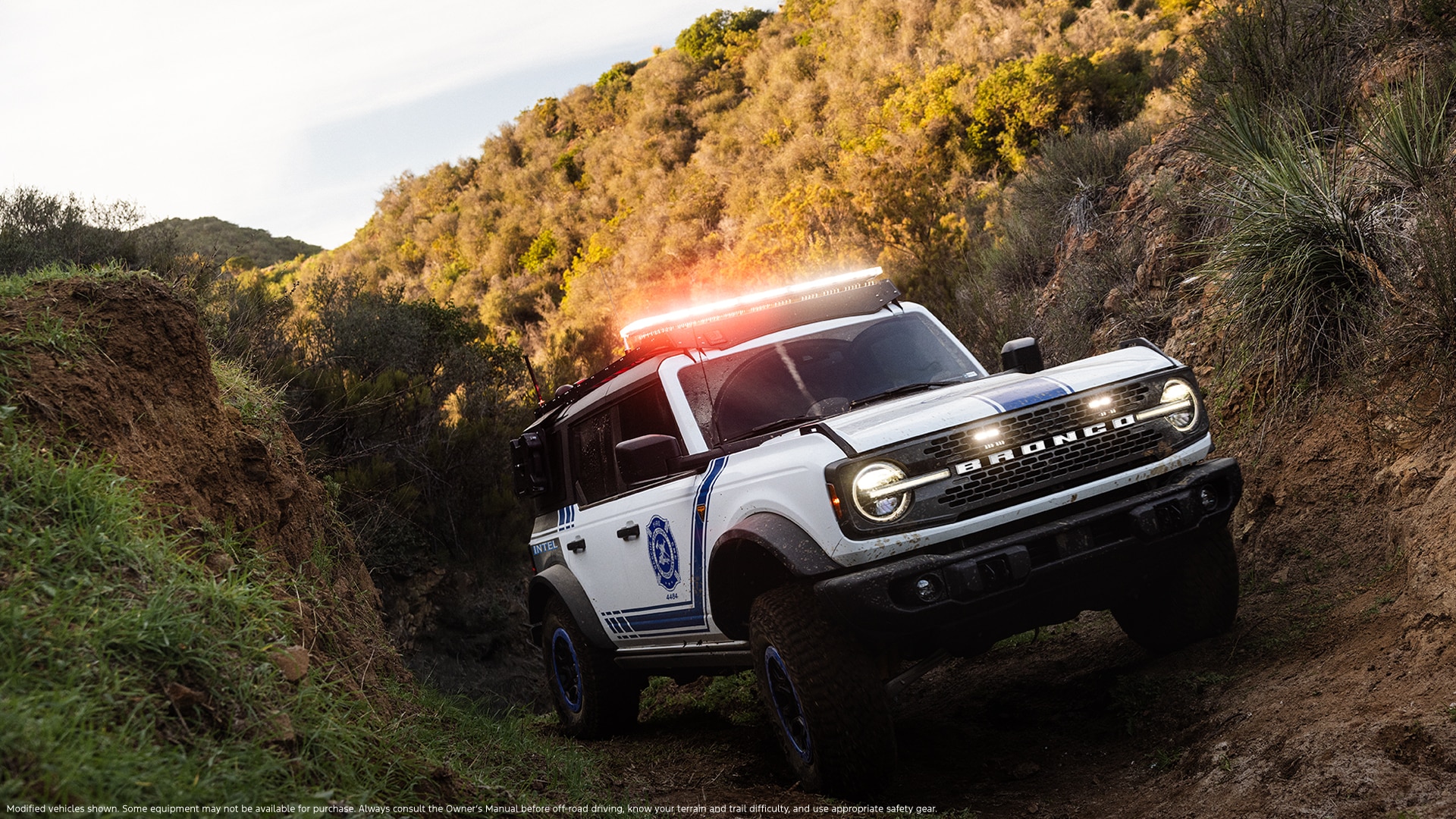 A Bronco with emergency lights on top drives off-road through a canyon.